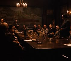 a group of people sitting around a table in a dark room with chandeliers