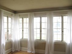 an empty room with white curtains and wood floors