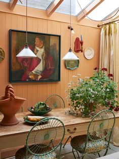 a dining room table with four chairs and a painting on the wall above it, along with potted plants