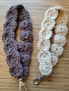 two crocheted lanyards are sitting on a wooden surface, one is brown and the other is white