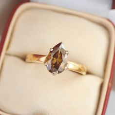 an engagement ring with a brown and white diamond on it in a red velvet box