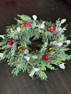 a christmas wreath with pine cones and red berries sits on a wooden floor next to a cell phone