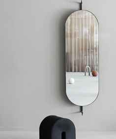 an oval mirror hanging on the wall next to a trash can and ball holder in front of it