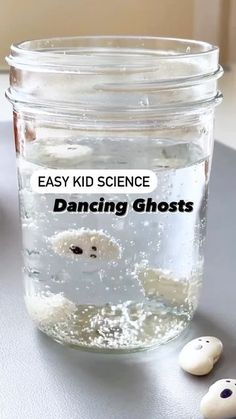 a glass jar filled with water next to two small white ghost heads on top of a table