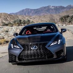 the front end of a gray sports car driving on a road with mountains in the background