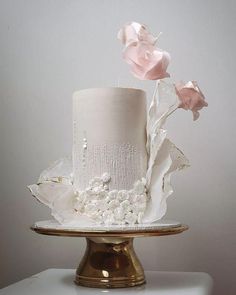 a three tiered cake with white frosting and pink flowers on top, sitting on a gold plate