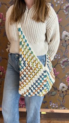 a woman holding a crocheted purse in front of a wallpapered background