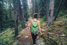 a woman with a green backpack is walking on a trail in the woods near rocks and trees