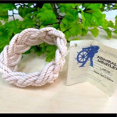 a white rope bracelet sitting on top of a wooden table next to a green plant