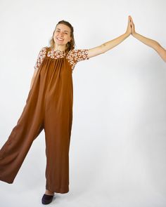 a woman in brown jumpsuits is holding her arms out to the side and smiling