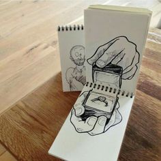 a hand holding a cell phone next to a notebook on a wooden table with drawings