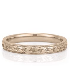 a gold wedding band with leaves on the side and engraving in the middle, sitting on a white surface