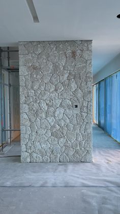 an empty room with a wall made out of rocks and blue doors in the background