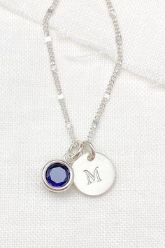 For her birthday, show her lots of love by gifting her a personalized piece of jewelry that she can treasure and wear daily. Her September birthstone, a sparkling lab-created blue sapphire, is back-set in sterling silver. This lovely centerpiece is complemented by a hand-stamped initial charm disc, customized with the letter of your choice.  These captivating charms dangle from a delicate, shimmering chain that fastens with a spring ring clasp. All elements of this stunning piece are meticulousl Blue May Birthstone Jewelry For Gift, Blue Jewelry Gift For May Birthstone, Blue Jewelry For May Birthstone Gift, Silver Necklace For May Birthstone Anniversary, Sterling Silver Sapphire Birthstone Necklace, Silver Necklace For Anniversary With May Birthstone, Personalized Blue Jewelry For May Birthstone, Personalized Blue May Birthstone Jewelry, Sapphire Birthstone Jewelry For Gifts