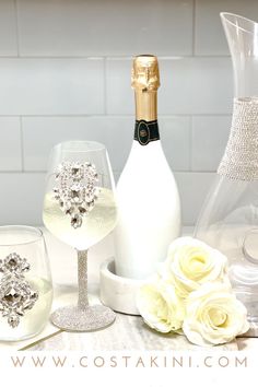 two wine glasses and a bottle of champagne on a table with white roses in the foreground