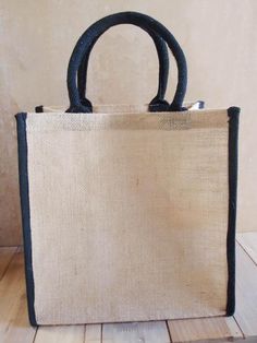 a white bag with black handles sitting on top of a wooden floor next to a wall