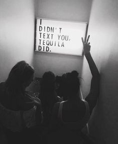 black and white photograph of three girls standing in front of a sign that says i didn't text you, tequila did