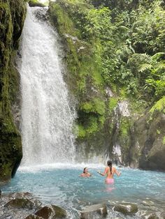 two people are in the water near a waterfall