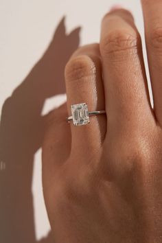 a woman's hand with a diamond ring on top of her finger, casting a shadow