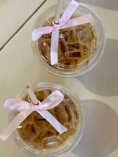 two cups filled with ice cream and some pink ribbon tied around the top, on a table