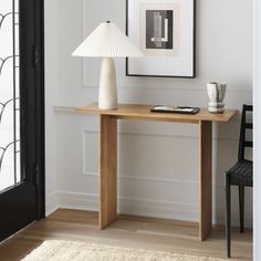 a white lamp sitting on top of a wooden table next to a black chair and framed pictures