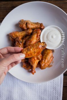 a person dipping sauce on top of chicken wings in a white bowl with a napkin