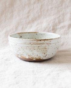 a white bowl with brown speckles on the rim sits on a light colored surface