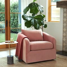 a living room with a pink chair and a large potted plant in the corner