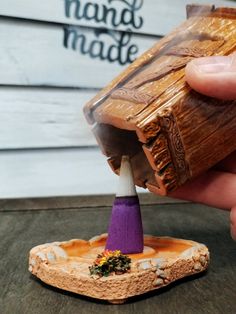 a hand holding a miniature wooden object with a purple cone on it's tip