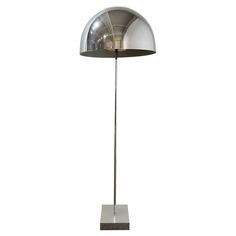 a metal floor lamp on a white background with the light reflecting off of it's base