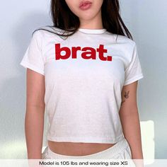 "Brat Baby Tee Charli XCX" Graphic Slogan Printed On Aesthetic Retro Vintage 90s Y2k Baby Tee Shirt with our own unique font.  🎨 Available in White, Light Pink, Light Blue, Navy, Black. If you need a different color, please let us know! (Ash, Red, Sport Grey & Green)  🎁 Our baby tees are perfect gift for her or him offering timeless fashion and versatility that anyone will cherish. Baby tees, popular in the '90s, have short sleeves and a slightly cropped body, giving a flattering feminine shap Pre-shrunk Stretch Tops For Streetwear, Stretch Grunge T-shirt For Streetwear, Grunge Stretch T-shirt For Streetwear, 90s White Stretch Tops, 90s Style White Stretch Tops, Stretch Pre-shrunk Tops For Streetwear, White Stretch 90s Tops, Red Fitted Grunge T-shirt, Y2k Fitted Logo Print Tops