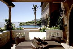 an outdoor dining area with table and chairs overlooking the water in front of a house