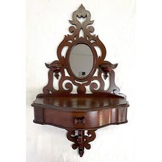 an ornate wooden shelf with a mirror on it's top, against a white wall