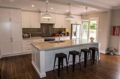 a large kitchen with white cabinets and wooden flooring, along with three bar stools