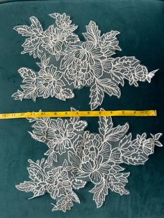 two pieces of white lace with flowers and leaves on green velvet, next to a measuring tape