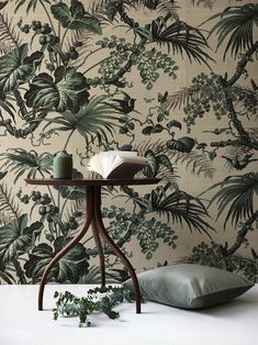 a table with a book on it next to a pillow and plant print wallpaper