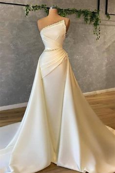 a white wedding dress on display in front of a gray wall with greenery hanging from it