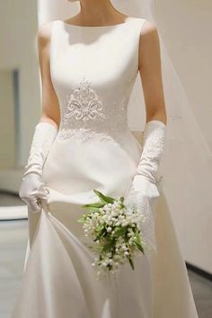 a woman in a white wedding dress holding a bridal bouquet and wearing long gloves