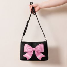 Jump into the pink bow aesthetic and coquette trend with this versatile pink bow crossbody bag with a black background. It has a modern and playful feel, which makes this handbag a great accessory and a perfect gift for every occasion. It's made of premium faux leather and features dark gray hardware. Thanks to the zip-top closure and multiple inside pockets, you can keep your essentials secure and organized. Transform this crossbody bag with removable wrist and shoulder straps to style it for d Rectangular Bags With Detachable Bow For Gifts, Rectangular Bag With Detachable Bow For Gifts, Rectangular Bag With Detachable Bow As Gift, Cute Pink Bag With Bow, Cute Black Shoulder Bag For Party, Chic Pink Shoulder Bag With Bow, Cute Black Shoulder Bag With Mobile Phone Pocket, Black Rectangular Bag With Bow, Cute Black Shoulder Bag With Detachable Strap