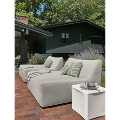 an outdoor couch with pillows on it in front of a black building and brick walkway