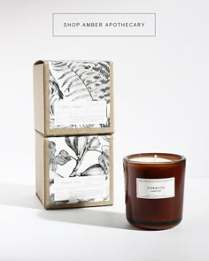 a candle sitting next to a box on a white background with the words shop amber apothecary