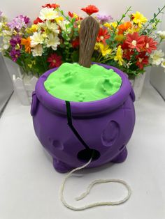 a purple and green toy sitting on top of a white table next to flowers with a wooden stick sticking out of it