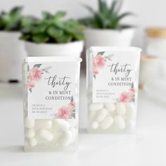 two packages of white and pink candy sitting on a table next to potted plants