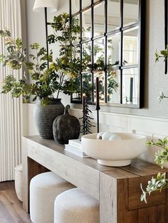 a table with two vases on top of it and some plants in front of the mirror