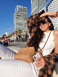 a woman is sitting on the curb with her hand in her hair and wearing sunglasses