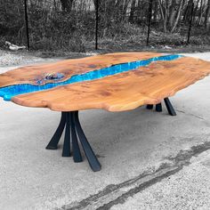 a wooden table with blue paint on it in the middle of a parking lot next to trees