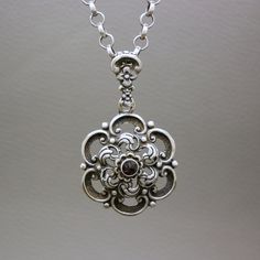 A gorgeous vintage silver necklace pendant with a small rose cut genuine garnet stone. The pendant is stylized as a flower. A great quality collectible Biedermeier style Dutch heritage jewelry item. You may choose to buy this pendant on its own, or with a matching 28 inches (72 cm) handcrafted antique sterling silver chatelaine chain, shown on the photos. The item will be shipped in a gift box. An excellent gift idea! Garnet is the birthstone of January. It is also traditionally known as the gem Antique Garnet Pendant Necklace, Elegant Vintage Charm Necklace With Flower Pendant, Elegant Vintage Charm Flower Pendant Necklace, Elegant Necklace With Vintage Flower Pendant, Elegant Vintage Flower Pendant Necklace, Ornate Sterling Silver Necklace With Vintage Charm, Elegant Antique Silver Flower Pendant Necklace, Elegant Antique Silver Necklace With Flower Pendant, Antique Silver Garnet Jewelry