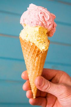 a hand holding an ice cream cone with pink and yellow toppings on top, against a blue background