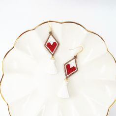 a pair of red and white beaded heart earrings on a plate with tassels