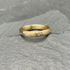 a yellow gold ring with five diamonds on it sitting on a gray stone surface in front of a grey background